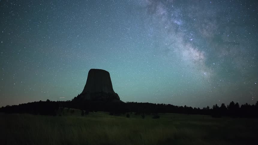 A stunning night-to-dawn timelapse shows the Milky Way galaxy moving across the starry sky above the silhouetted Devils Tower National Monument