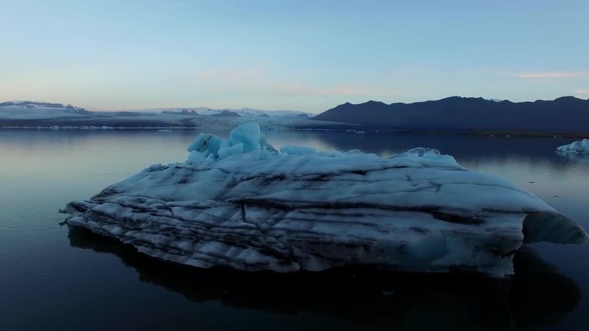 An icy glacier sits in a lake at sunset