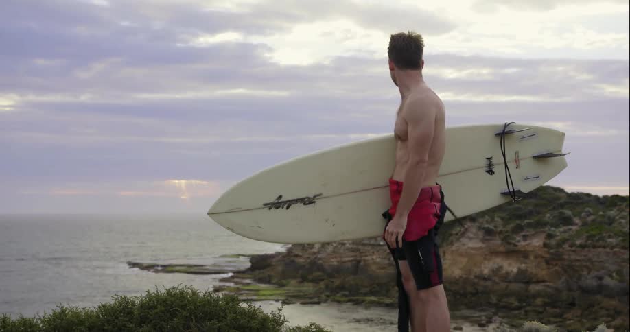 Man holding a surfboard looks out at the water