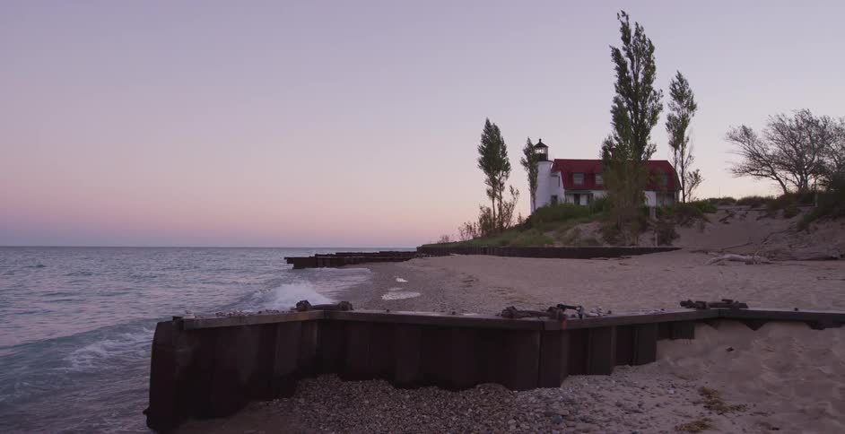 A serene view of the Point Betsie Lighthouse on the shores of Lake Michigan as gentle waves crash against the sandy beach at dusk