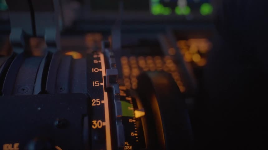 A detailed close-up view of an airplane's throttle quadrant and controls illuminated in a dark cockpit at night