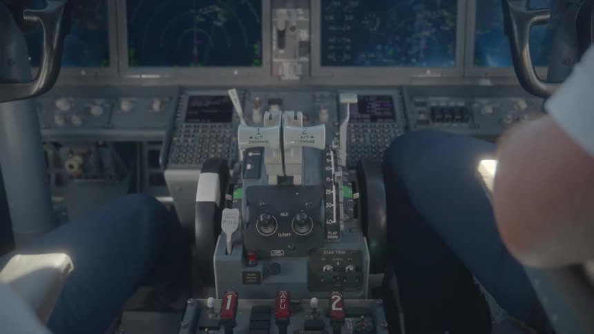 Over-the-shoulder view of two pilots operating the controls and throttle quadrant in a commercial airliner cockpit