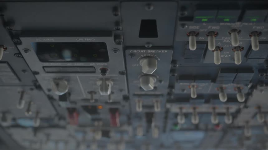 A low-angle close-up of the overhead control panel and circuit breakers inside an airplane cockpit during a turbulent flight
