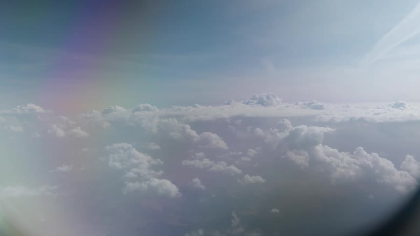 A serene aerial view of white clouds and blue sky slowly revealed from behind an airplane window frame
