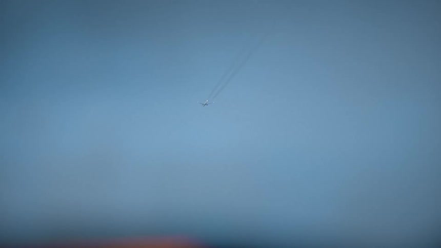 Low angle view of a jet leaving a vapor trail as it soars through the hazy blue sky