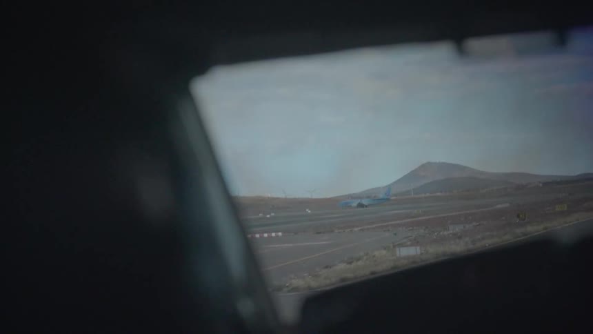A passenger airplane taxis on a runway at a remote airport with hills in the background, viewed from inside another plane