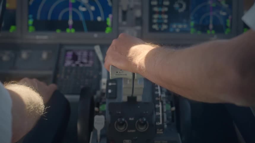 An over-the-shoulder view of a pilot holding the throttle levers in a modern aircraft cockpit