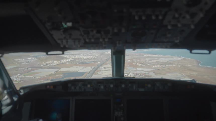 A blurry view from inside an airplane cockpit as it flies over a coastal city and landscape on approach