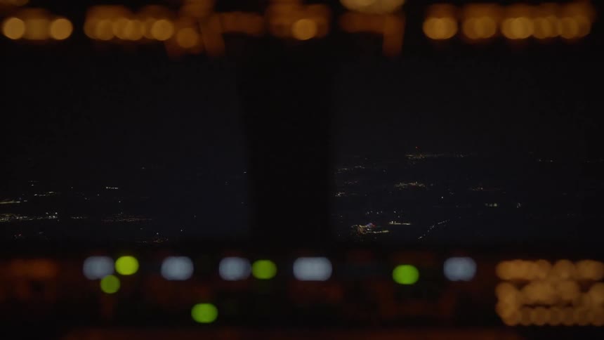 An out-of-focus view from an airplane cockpit flying over a city at night, with the instrument panel creating bokeh lights