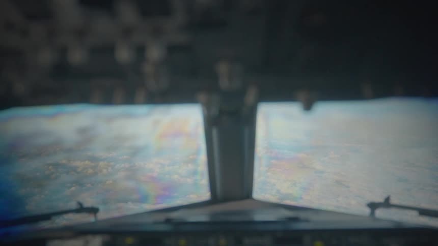 An out of focus point of view shot from an airplane cockpit flying high above the clouds
