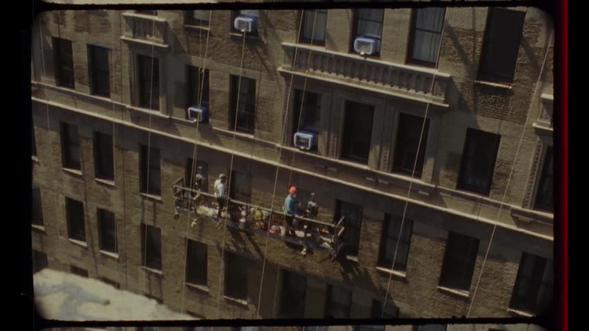 Archival footage shows two window washers ascending a tall brick building on a scaffold, revealing the New York City skyline