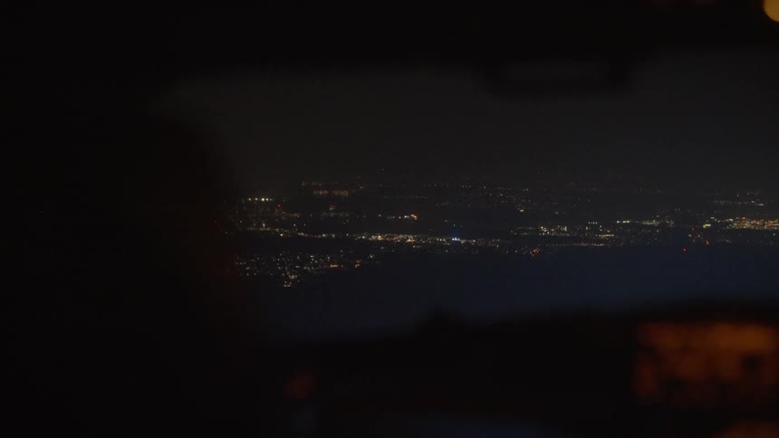 Over-the-shoulder view from an airplane cockpit looking out over the sprawling city lights during a night flight