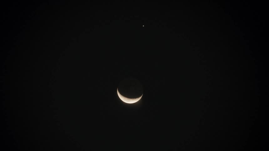 A beautiful crescent moon and a single bright star illuminate the dark, peaceful night sky