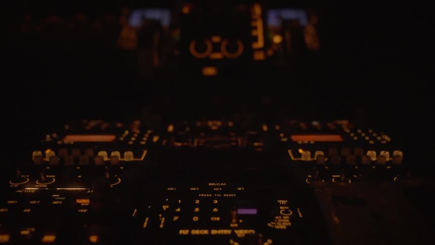 A dark airplane cockpit with glowing orange instrument panels and blinking lights during a night flight