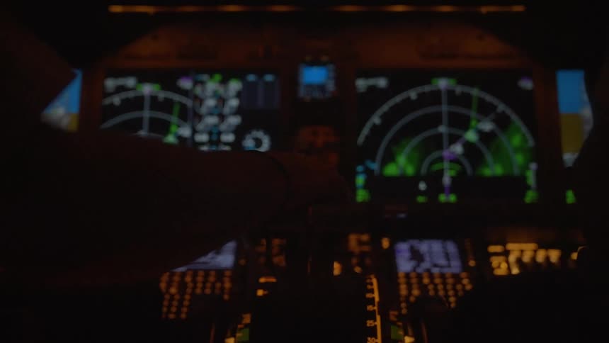 An out-of-focus shot of an airplane's control panel and navigation screens glowing in a dark cockpit at night