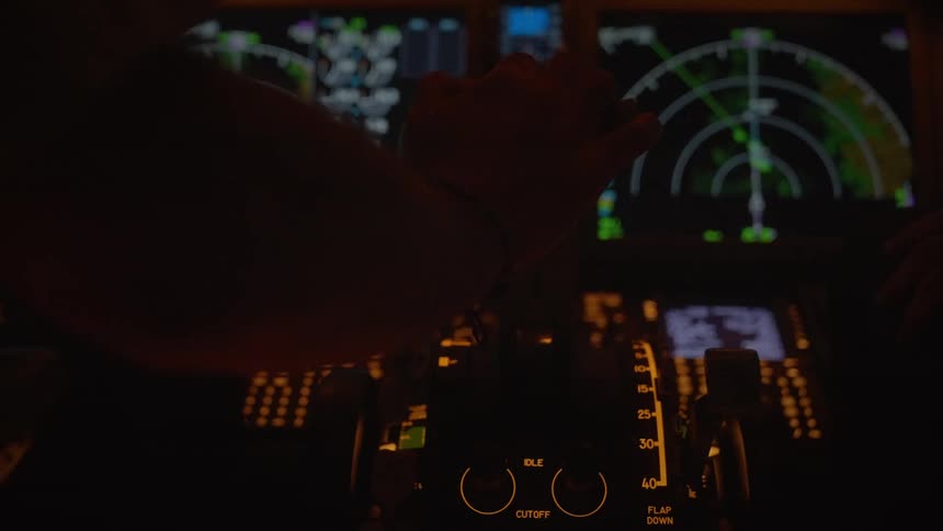 A close-up shot of a pilot's hand operating the throttle inside a commercial airplane cockpit during a night flight
