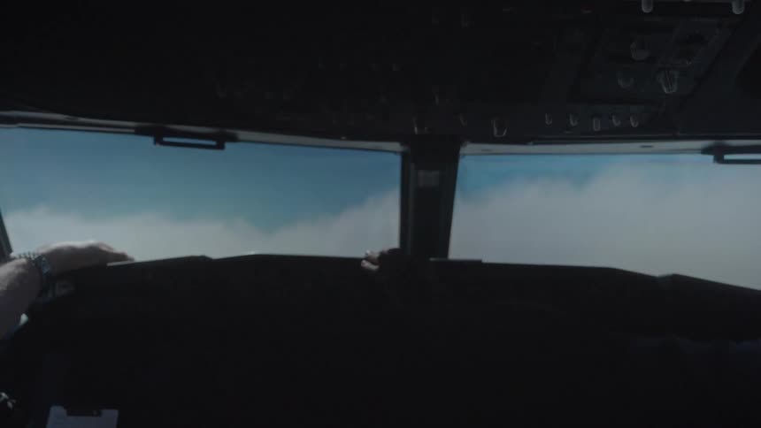 A tense POV from inside an airplane cockpit as it flies through thick, disorienting cloud cover before emerging into the sky