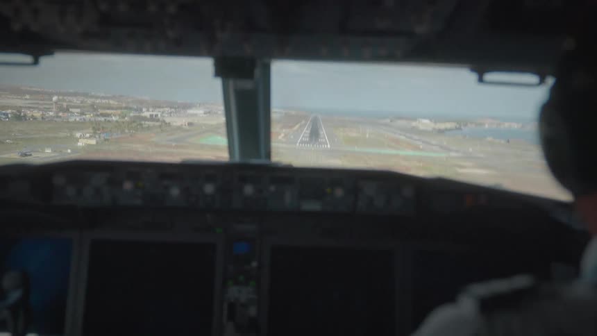 From the cockpit's point of view, a commercial airplane piloted by a professional descends and lands smoothly on an airport runway by the sea