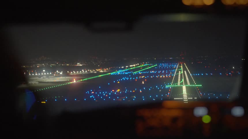 From the cockpit, an airplane makes its final descent onto a brightly illuminated airport runway for a night landing