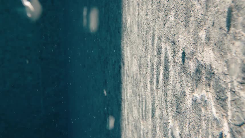 A minimalist vertical view of light and shadow on a submerged concrete wall as bubbles rise