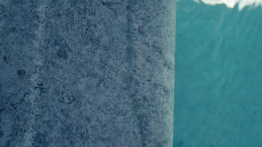 A vertical, abstract view of water flowing over the edge of a stone infinity pool