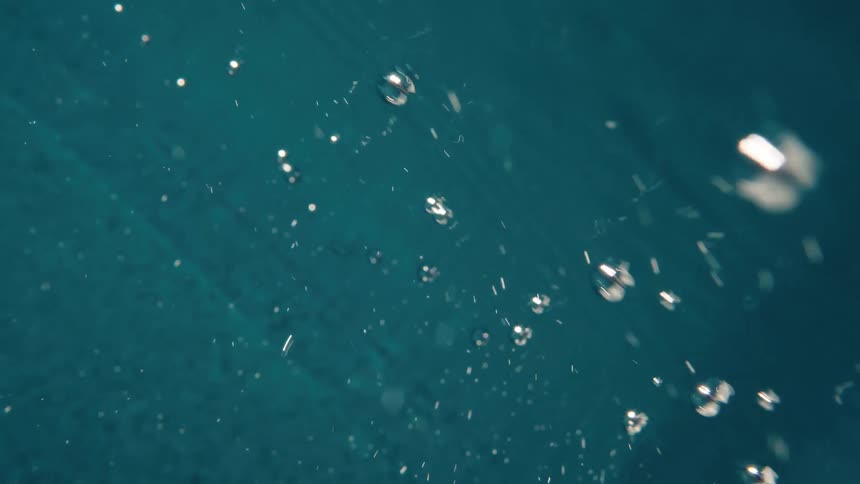 An abstract slow-motion view of shimmering air bubbles rising through deep teal water
