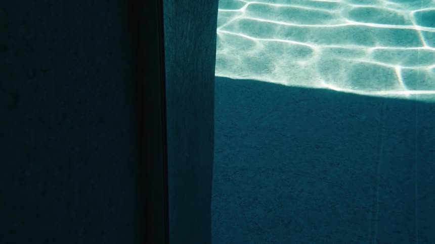 Calming ripples and sunlight reflections dance at the bottom of a teal-colored swimming pool beside a shadowy edge