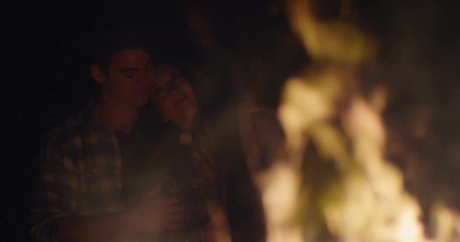 A man and woman cuddle next to a bonfire
