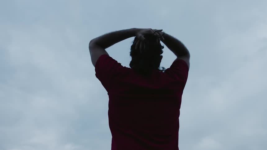 A man pulls back his hair while standing outside