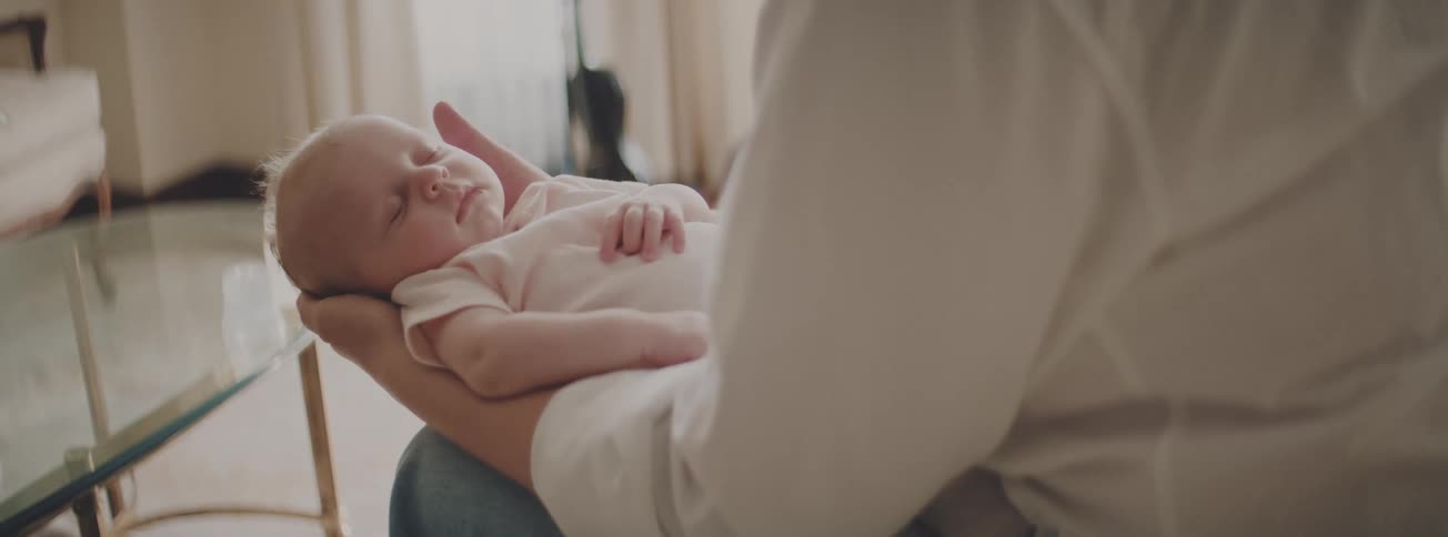 A gentle father cradles his newborn baby, who is sleeping peacefully in his arms in a warm, sunlit room