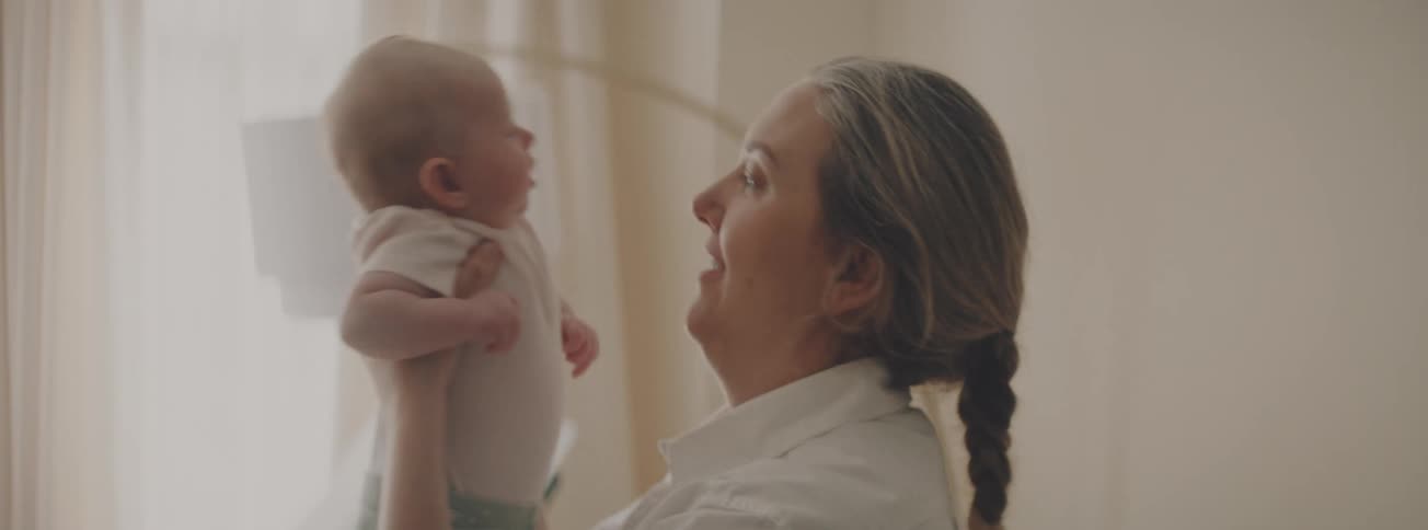A tender moment between a mother and her newborn baby as she holds, kisses, and talks to them in a sunlit room