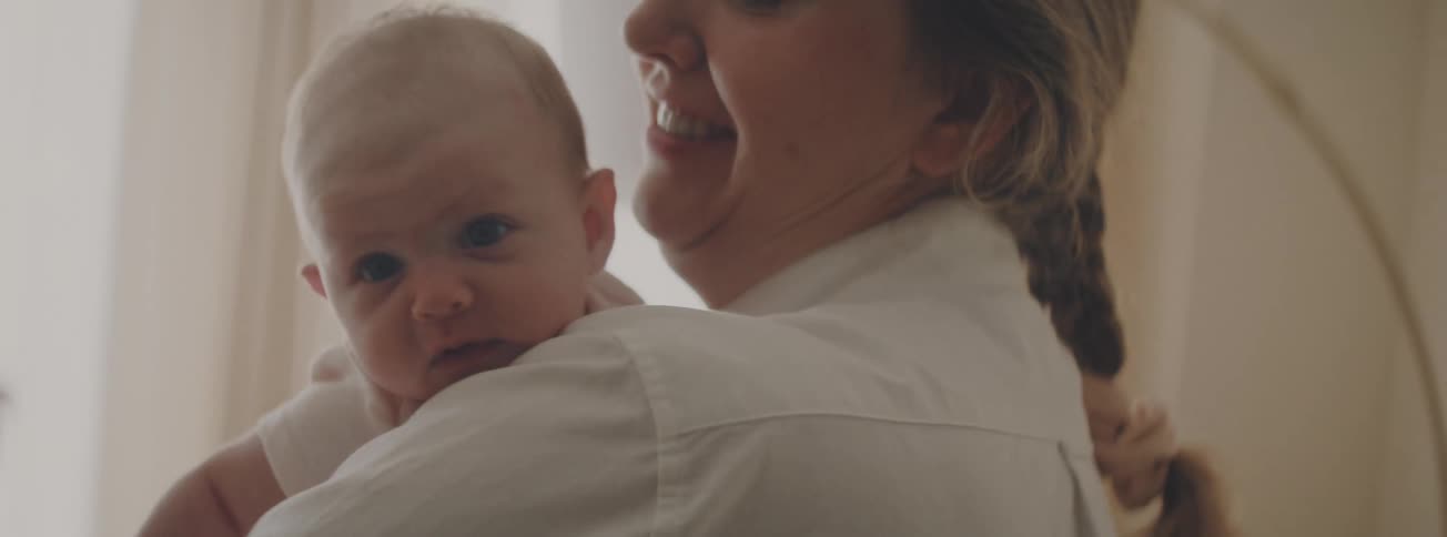 A happy mother smiles and kisses her sleepy newborn baby on the head as she holds them over her shoulder