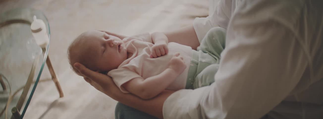 A newborn baby sleeps peacefully in the loving and gentle arms of a parent
