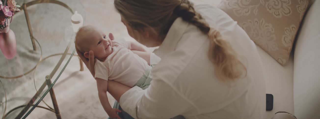 A tender moment as a mother holds her smiling newborn baby in a bright living room