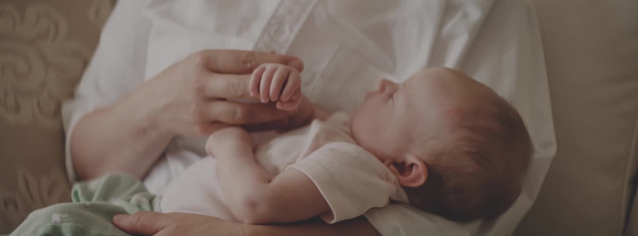 Close up of a parent's hand gently holding their sleeping newborn baby's tiny hand