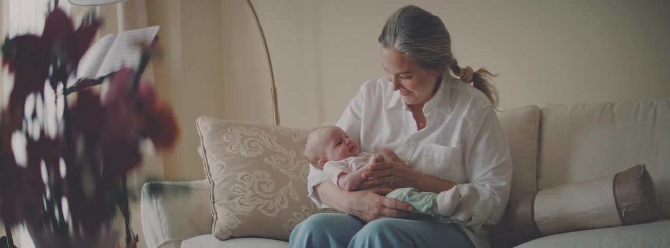 A happy mother gently holds and caresses her newborn baby while sitting on the sofa in their cozy living room
