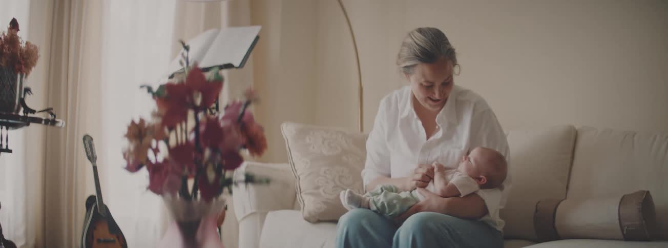A gentle mother lovingly holds her newborn baby in her arms while sitting on a cozy couch at home