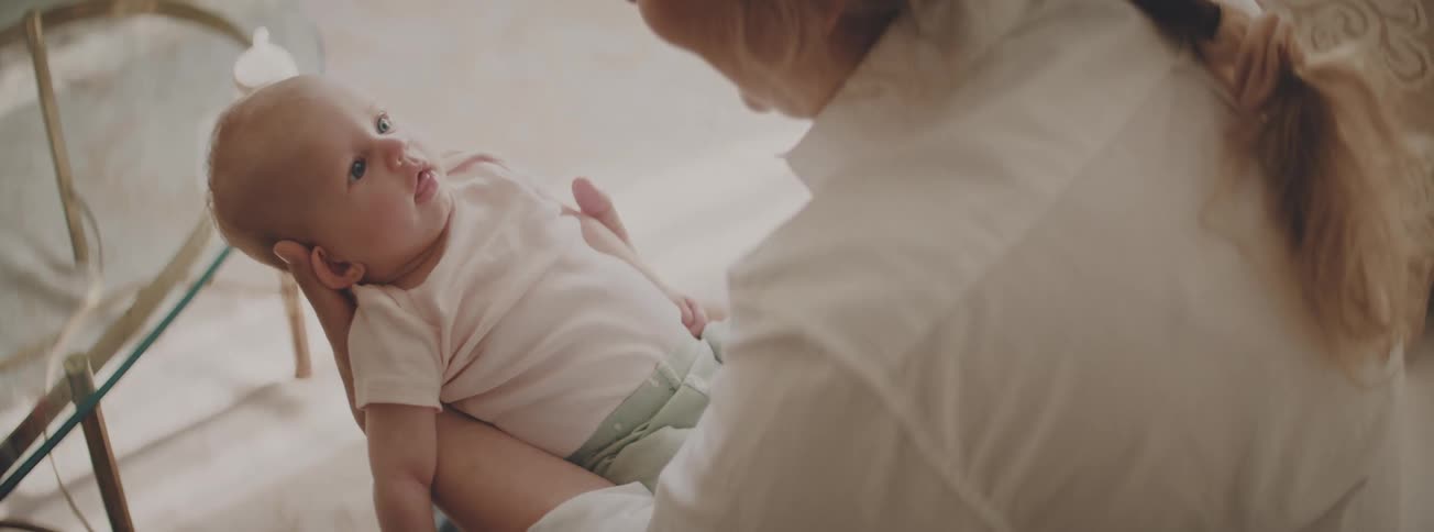 Over-the-shoulder shot of a loving mother holding her newborn baby who smiles brightly up at her