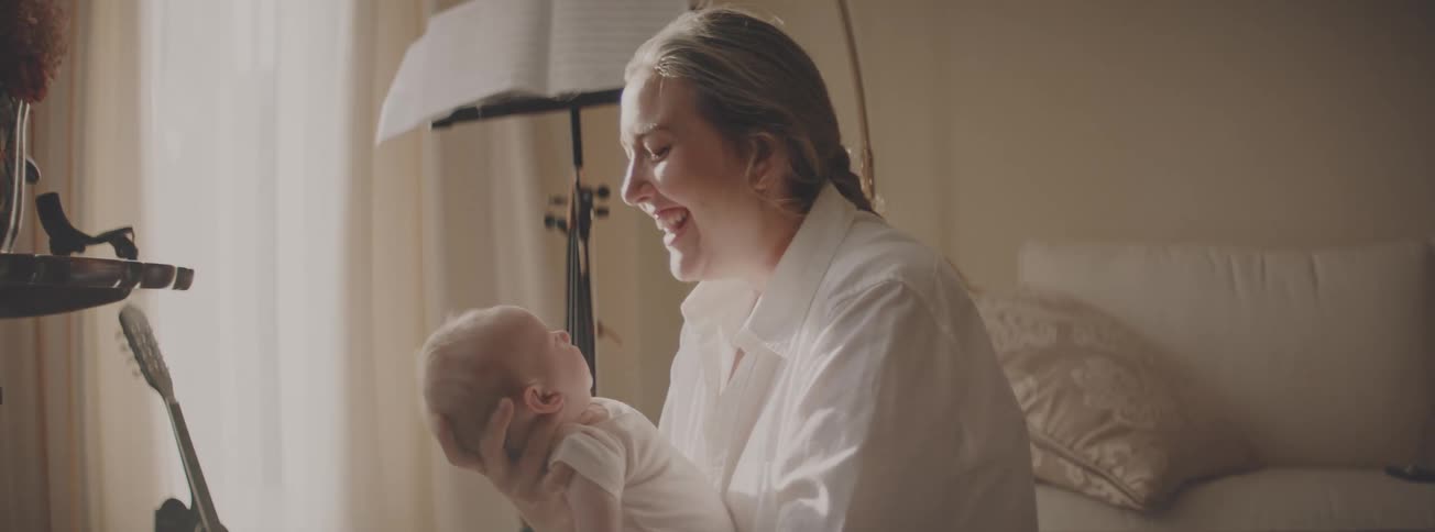 A happy mother smiles lovingly at her newborn baby while holding them in a warmly lit room