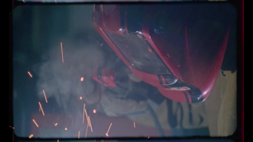 A vertical close-up of a welder in a red helmet working as sparks fly, captured on vintage film