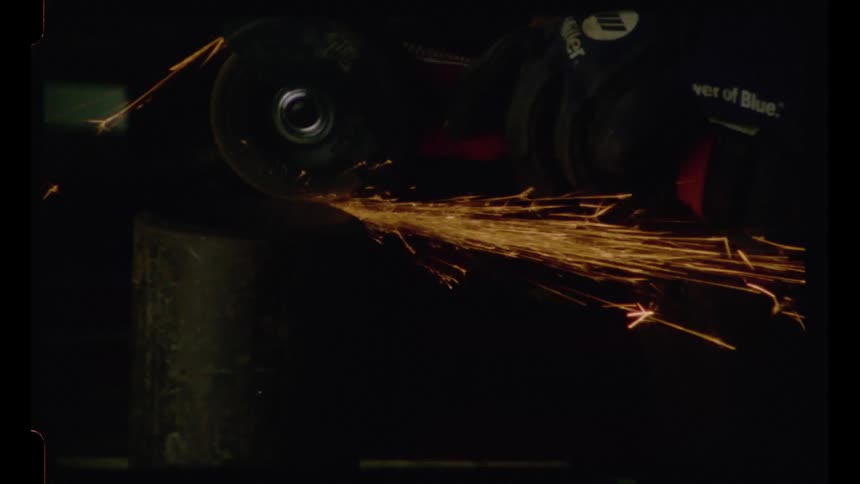 Authentic 16mm film captures the intense sparks flying from an angle grinder cutting metal in a dark industrial setting