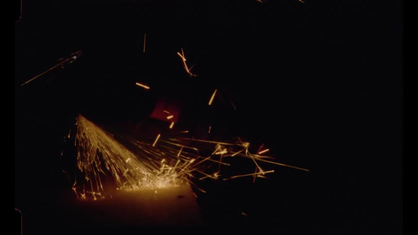 Vintage 16mm film footage shows a shower of sparks from a metal grinder in slow motion against a black background
