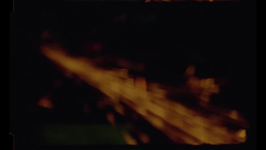 Sparks fly from a metal grinder in a dark workshop on grainy vintage film