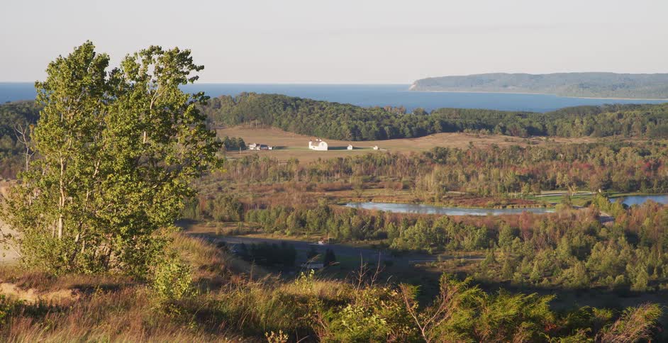 A scenic high-angle view of a rural valley with a distant white barn and a large lake on the horizon