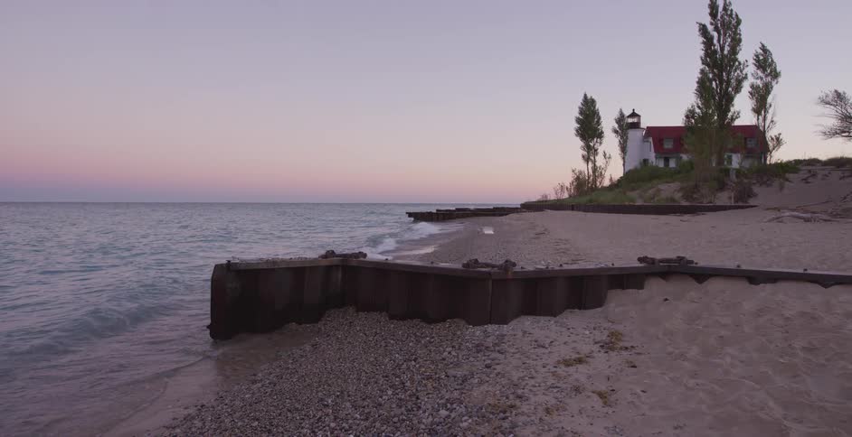 A tranquil view of gentle waves lapping the shore of a sandy beach with a picturesque lighthouse in the background at sunset