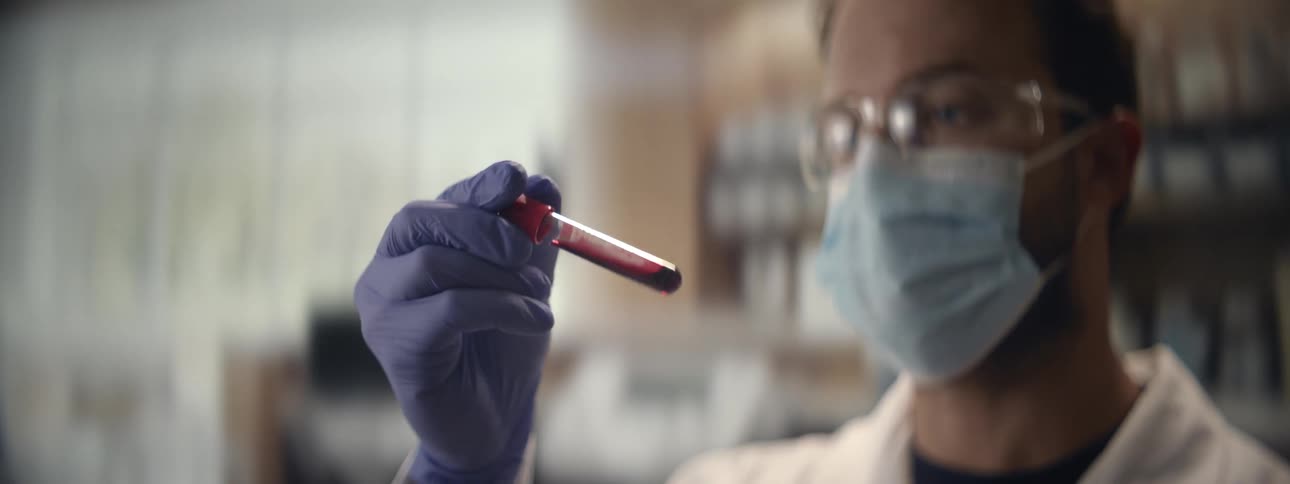 A medical researcher wearing protective gear analyzes a vial of blood in a laboratory