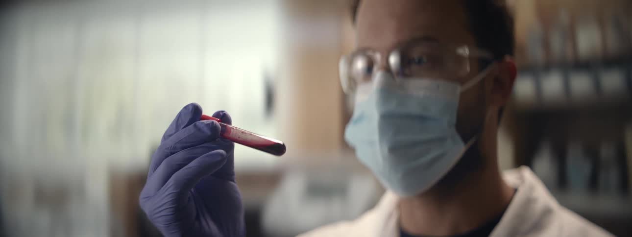Close up of a focused scientist in protective gear inspecting a vial of blood in a medical laboratory