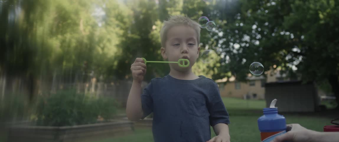 Toddler blows bubbles in a backyard