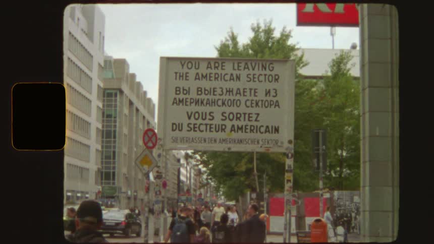 Vintage film footage captures the historic "You are leaving the American Sector" sign at Checkpoint Charlie in Berlin
