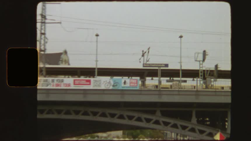 Vintage 8mm footage shows a yellow train crossing a bridge and arriving at Berlin Friedrichstraße station
